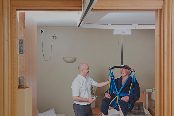 A patient using a fixed ceiling lift with a woman assisting